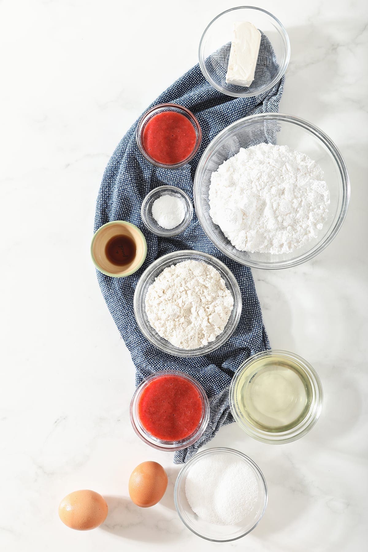 Ingredients for strawberry cupcakes on a dark blue towel on marble