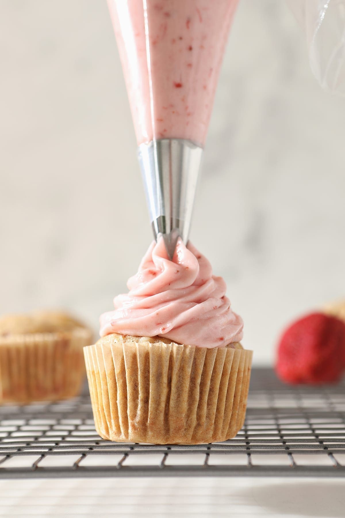 Strawberry Cream Cheese Frosting is swirled on top of a Strawberry Cupcake on a wire cooling rack