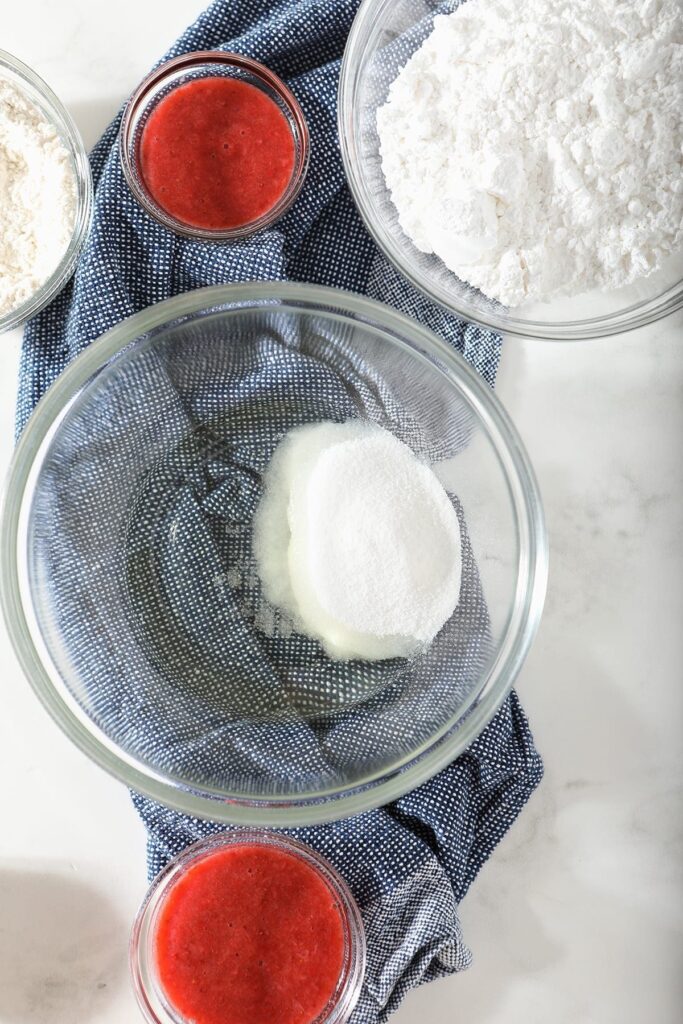 Oil and sugar in a glass bowl next to other bowls of cupcake ingredients