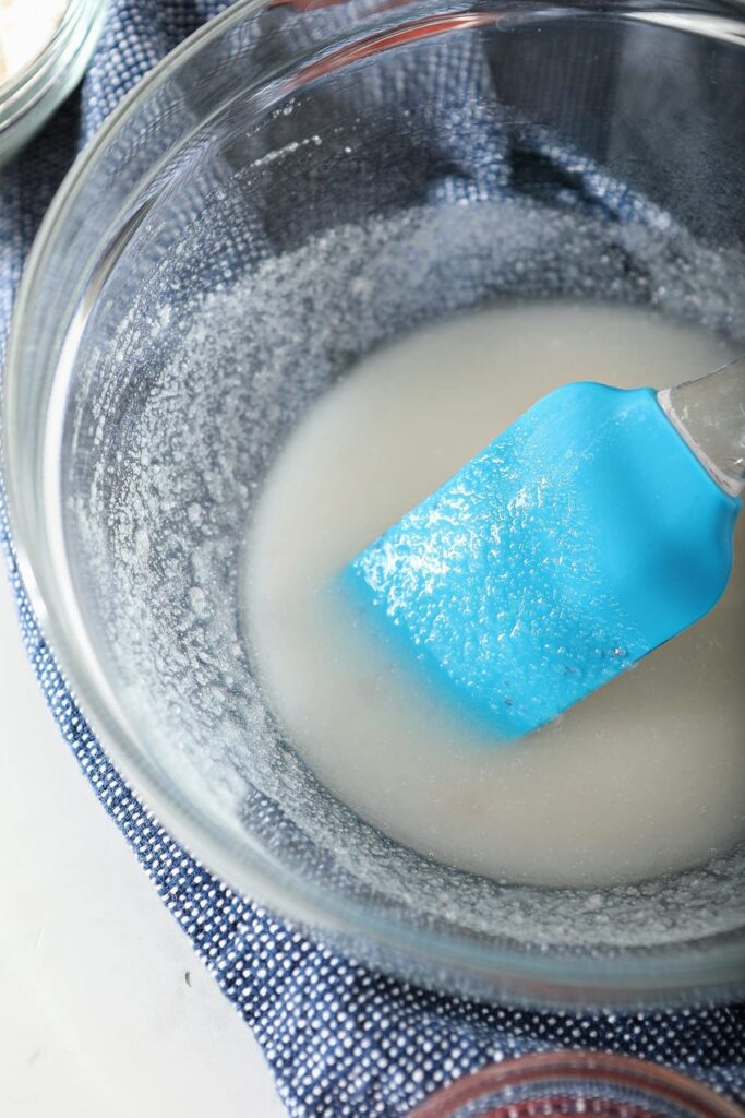 A blue spatula stirs sugar and oil together in a glass bolw