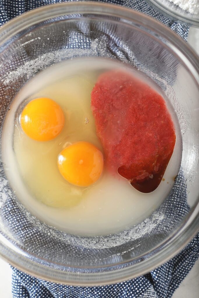 Fresh strawberry puree, eggs, sugar, oil and other wet ingredients in a glass bowl