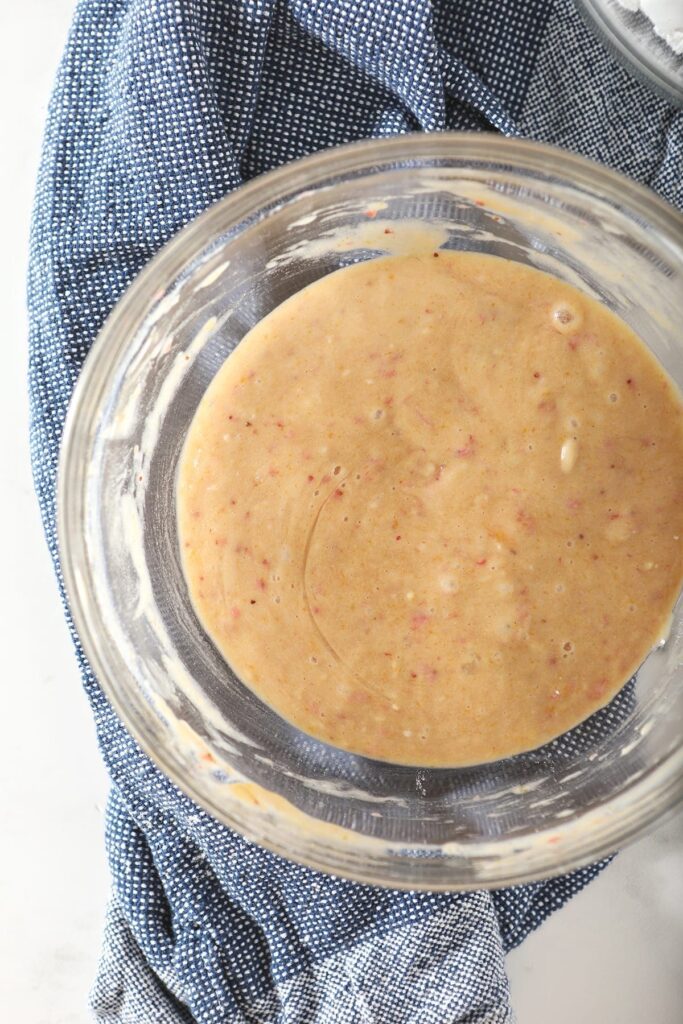 Strawberry cupcake batter in a glass bowl on a dark blue towel