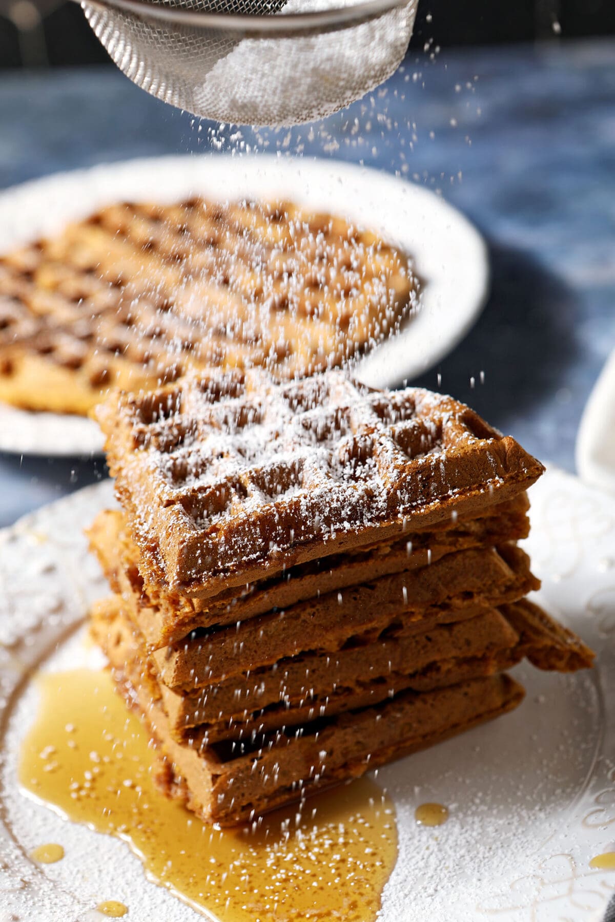 Powdered sugar sprinkles down on top of a stack of pumpkin waffles