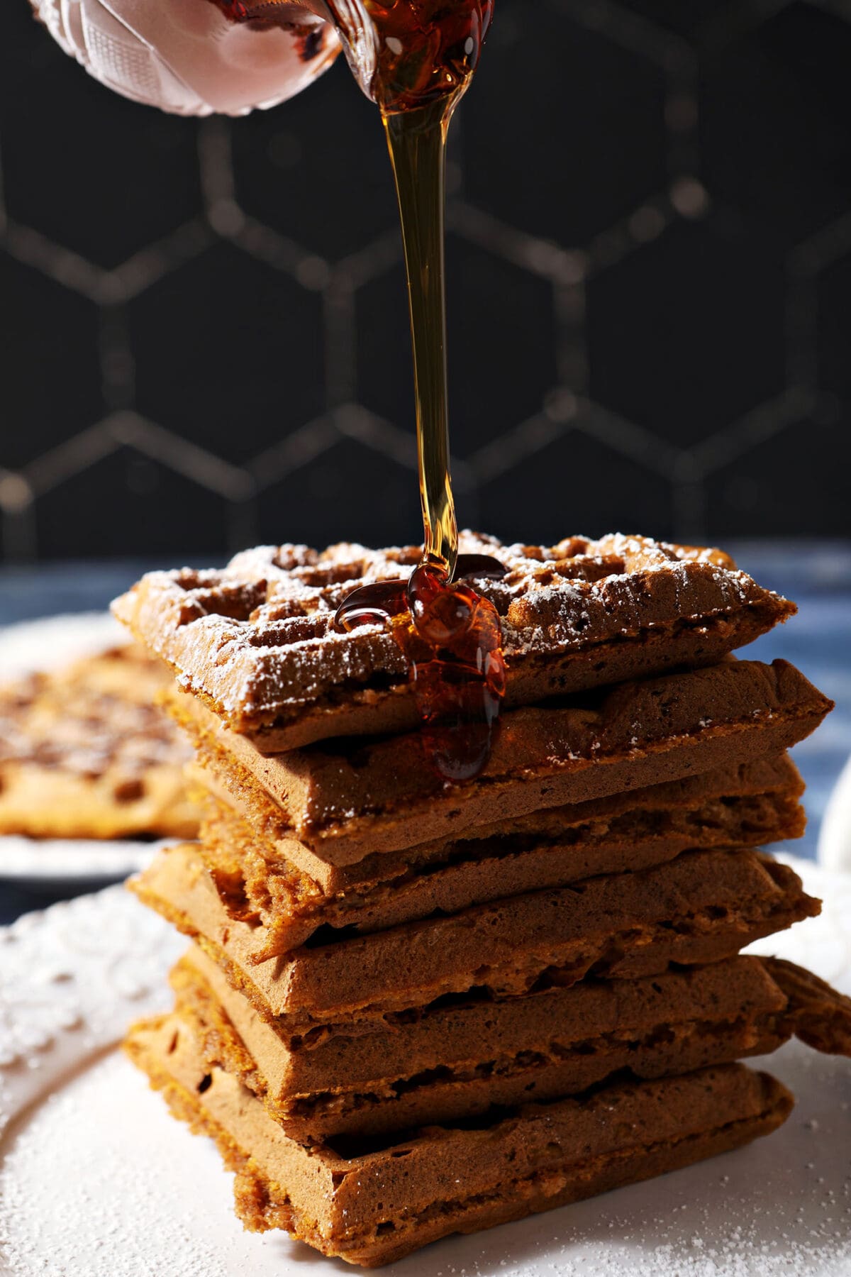 Syrup pours onto a stack of pumpkin waffles on a white plate