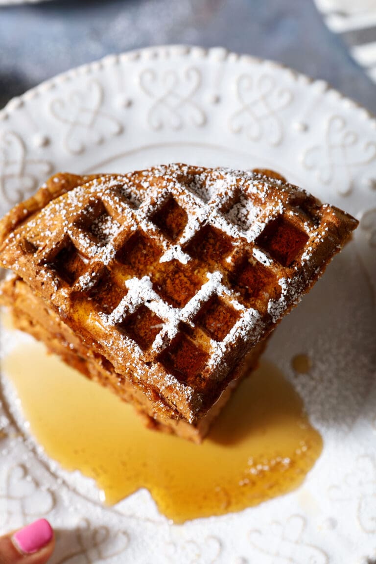 Overhead of a stack of pumpkin waffles topped with powdered sugar and maple syrup
