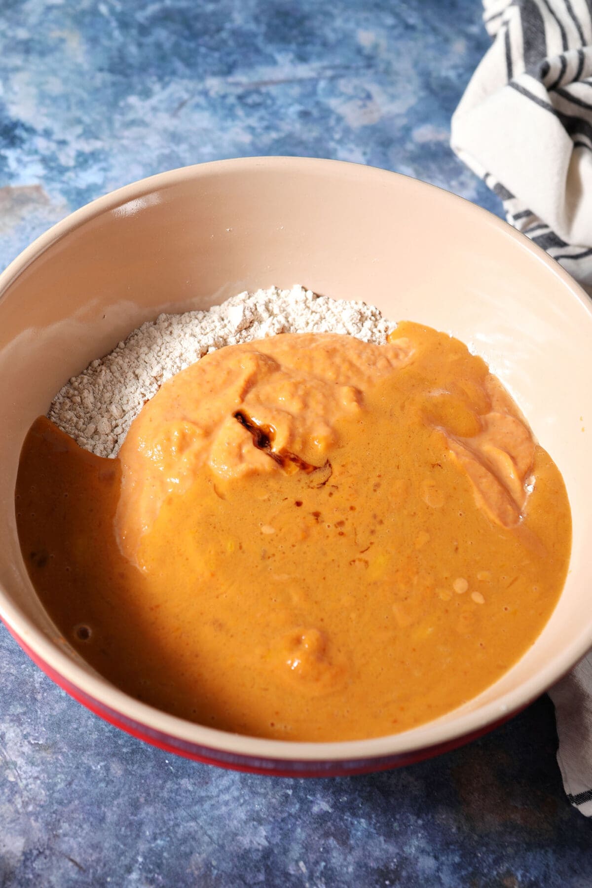 Wet ingredients sit on top of dry ingredients in a bowl on a dark blue surface before mixing
