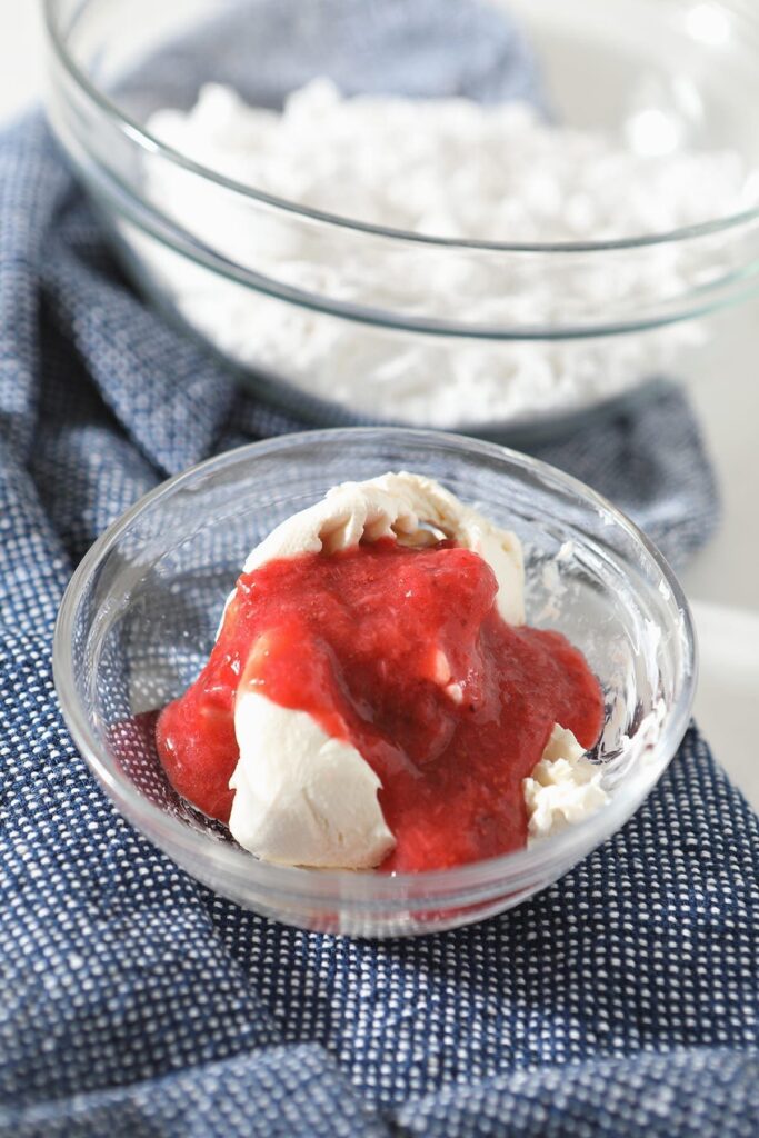 Strawberry puree on top of cream cheese in a glass bowl on a blue towel