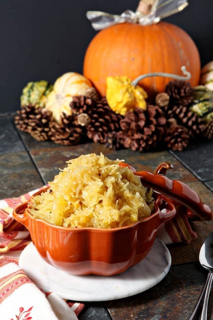 Orange bowl of spaghetti squash on linens in front of autumn décor 