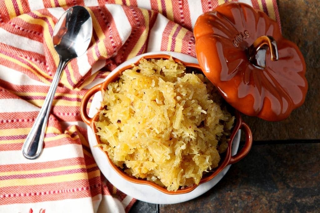 Overhead close up of spaghetti squash in orange pumpkin bowl with linens