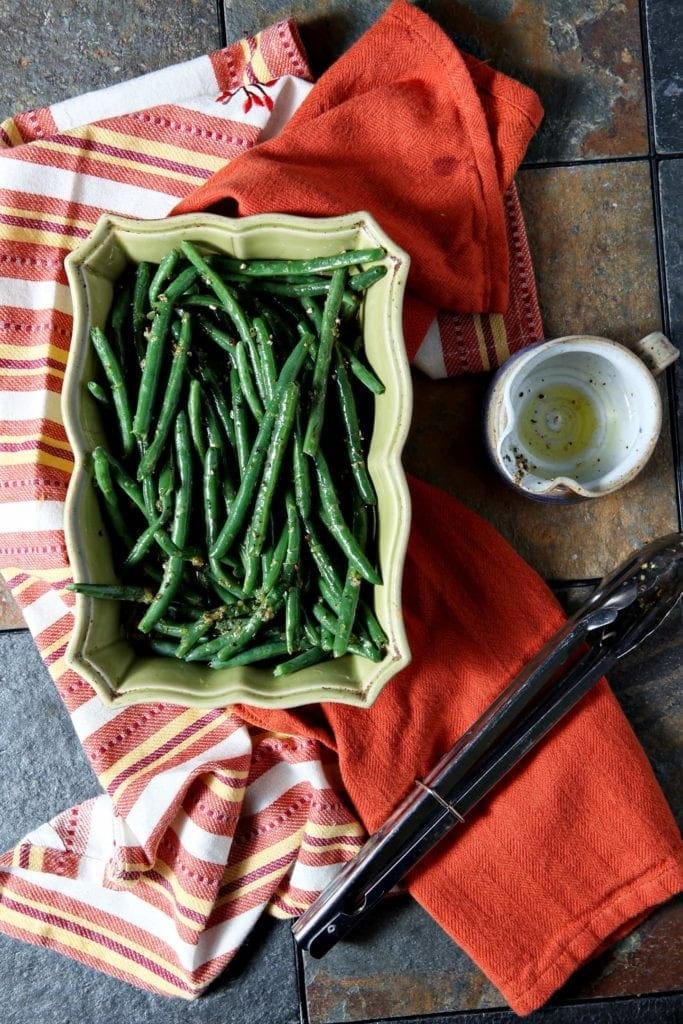 Overhead view of lemon pepper green beans in serving dish surrounded by linens