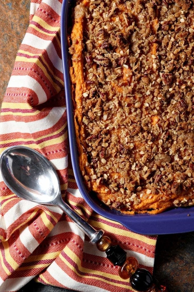 A purple casserole dish holds a Bourbon Sweet Potato Casserole, displayed with an orange towel for serving