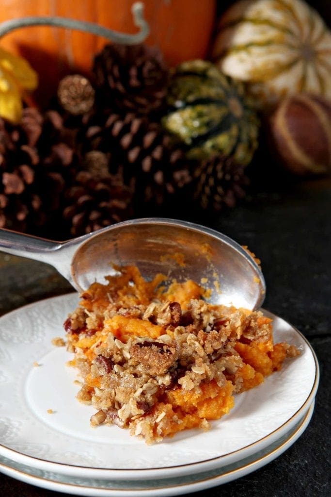 A metal spoon scoops a serving of sweet potato casserole onto a small white plate