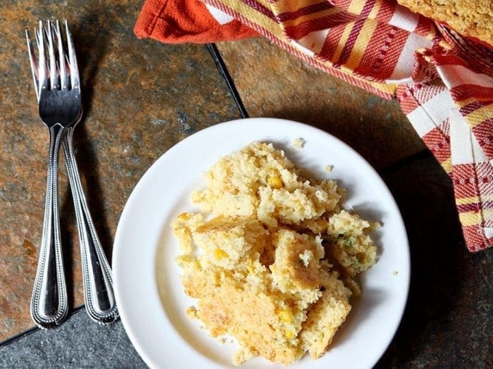 A plate of Creamed Cornbread Casserole, shown from above, on a dark background
