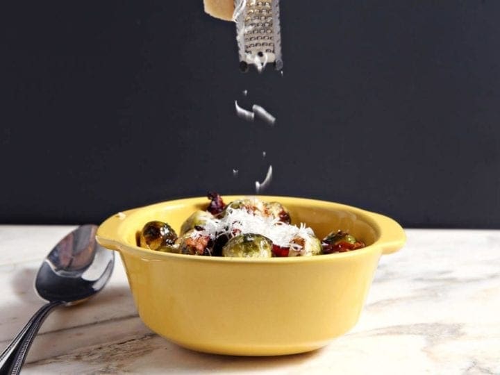 Grated cheese sprinkling on top of brussels sprouts in yellow dish