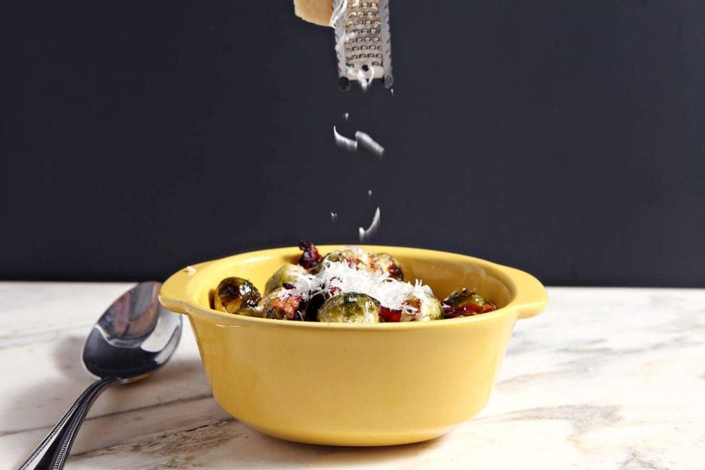 Grated cheese sprinkling on top of brussels sprouts in yellow dish 