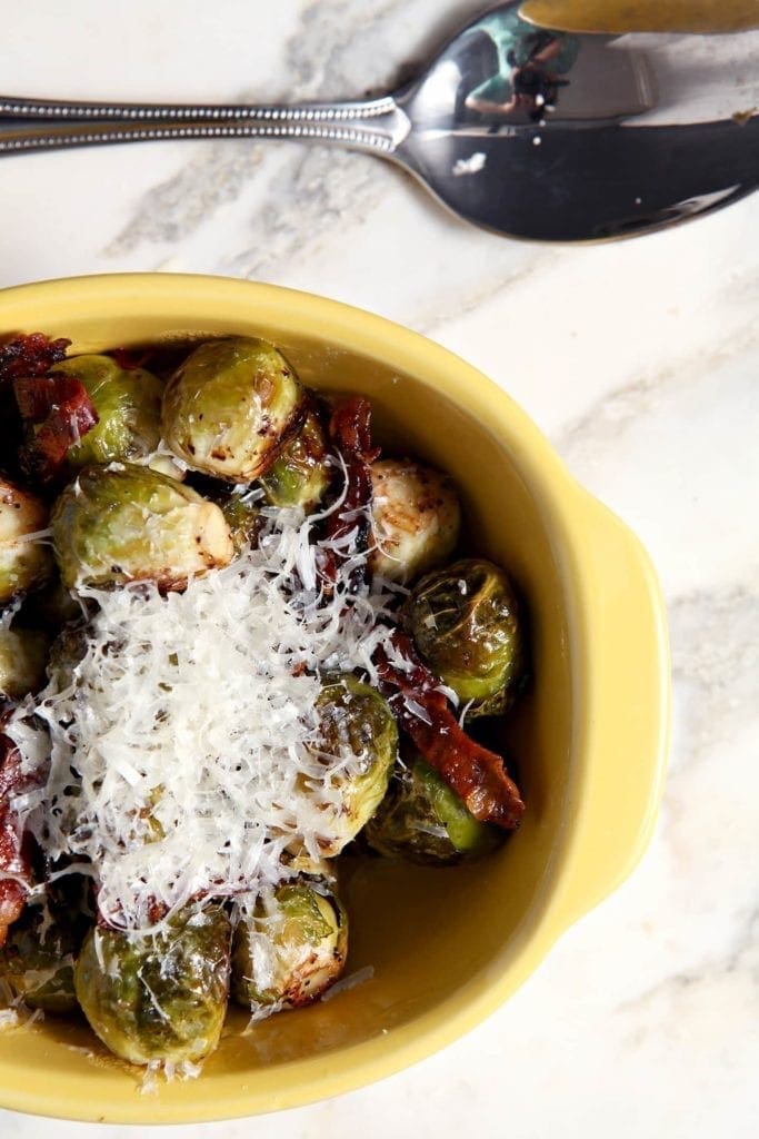 Overhead view of cheese on top of brussels sprouts in yellow dish 