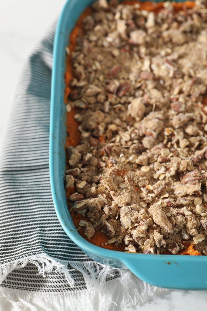 Close up of the Bourbon Sweet Potato Casserole in a blue dish on a grey striped towel before baking