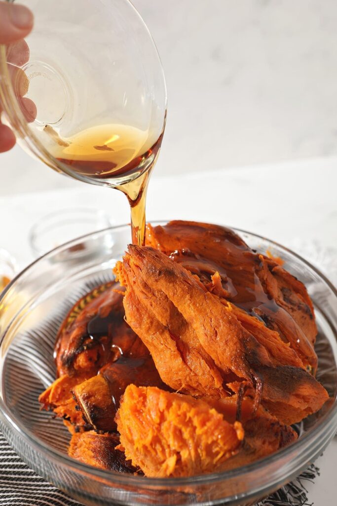 Maple syrup is poured on top of baked sweet potatoes in a bowl