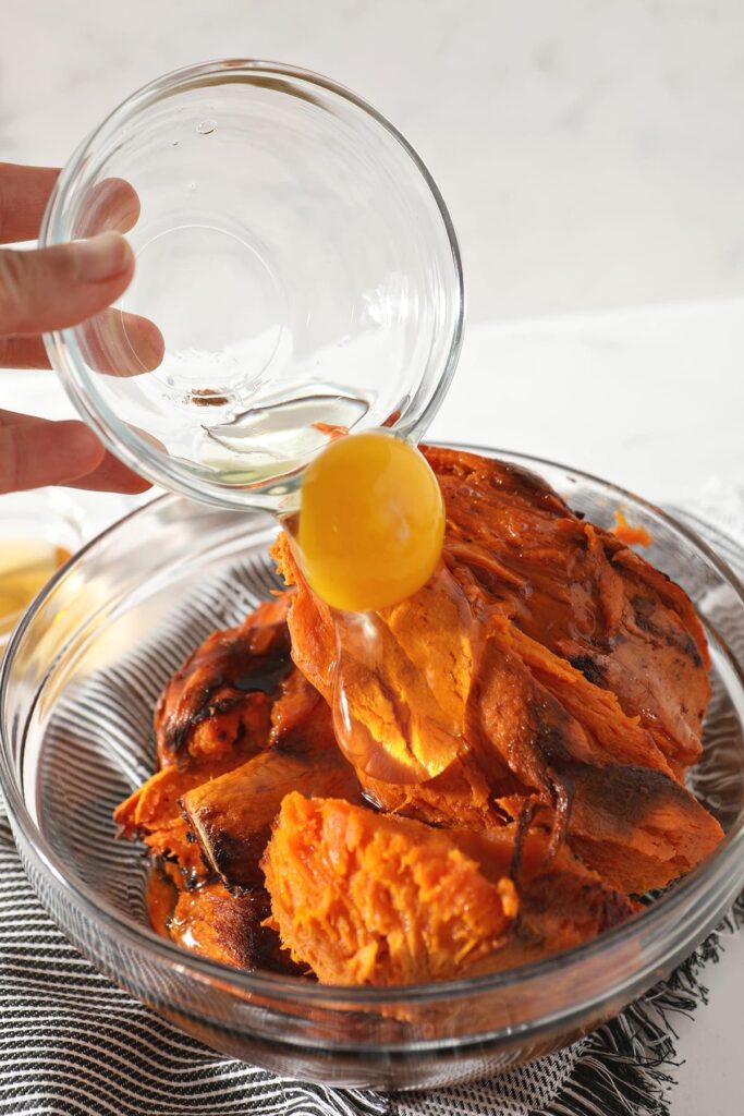 A whole egg is poured on top of baked sweet potatoes in a bowl