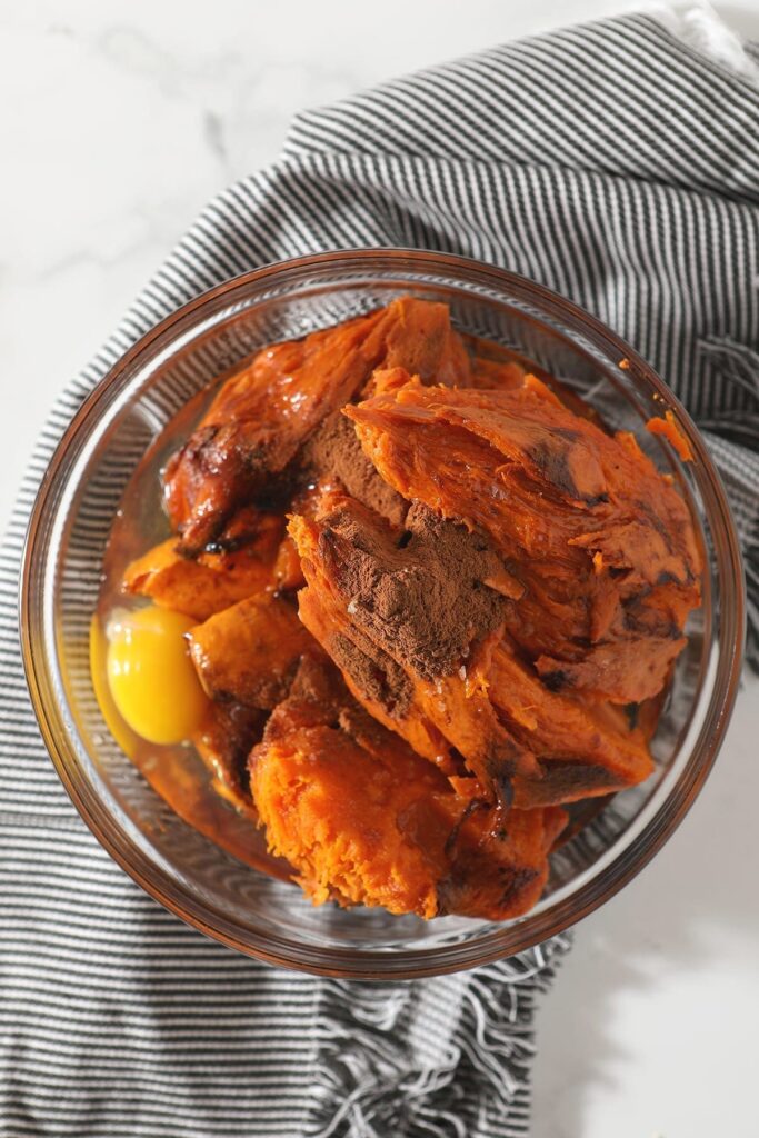 Bourbon Sweet Potato Casserole ingredients in a glass bowl on top of a striped grey towel