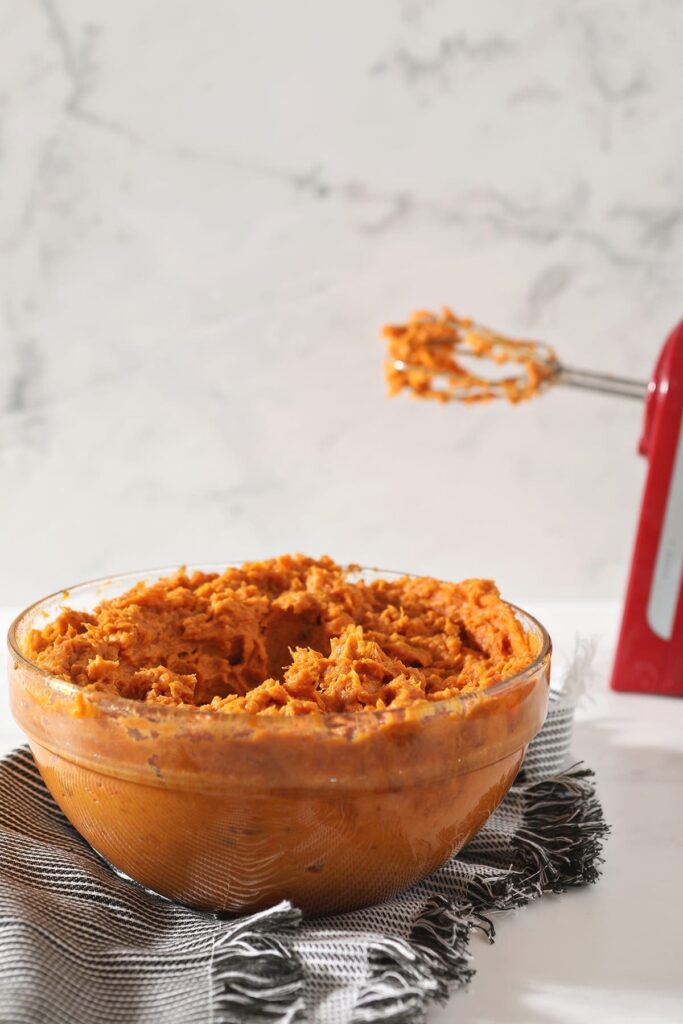 The blended sweet potato mixture on a striped grey towel with a red hand mixer behind it