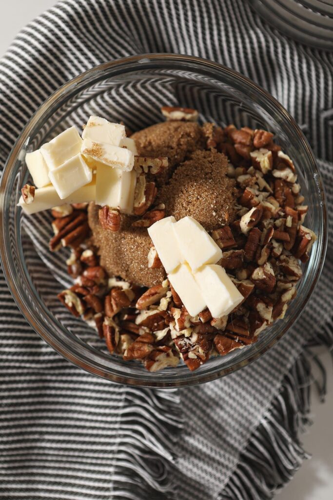 Sugar, butter, flour and pecans in a bowl before blending on a grey towel