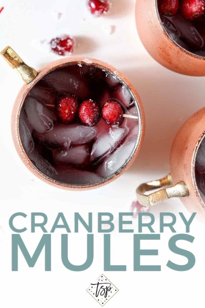 Pinterest image for Cranberry Mules, featuring a close-up overhead shot of the drink in copper mugs, garnished with sugared cranberries