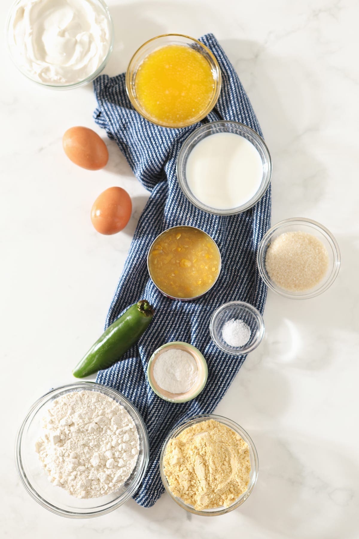 Cornmeal, flour, sour cream, butter, eggs, jalapeno and more in bowls on top of marble before the casserole is mixed