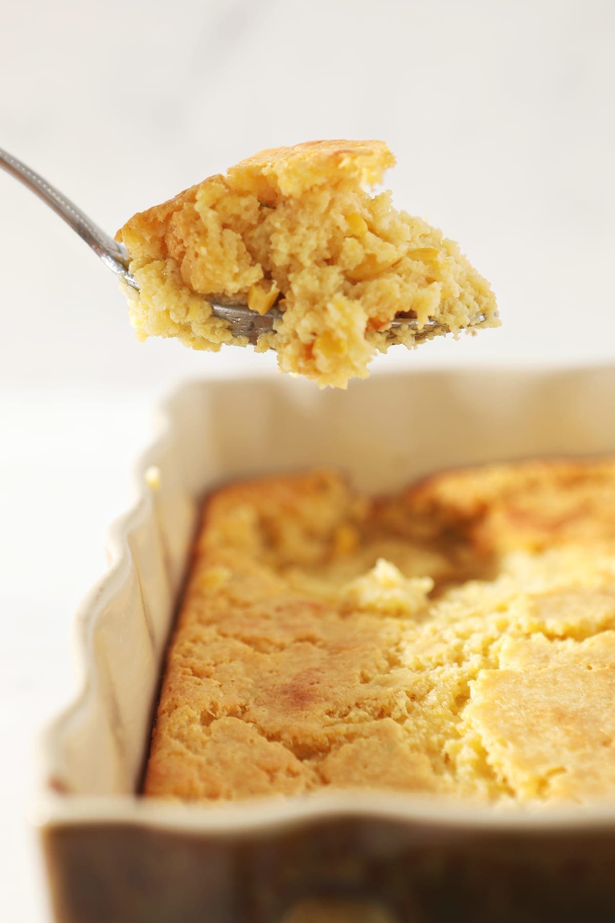 Creamed Cornbread Casserole lifted out of the dish with a silver spoon