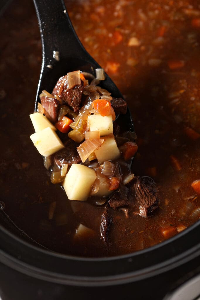 A spoon lifts a serving of beef stew out of a slow cooker