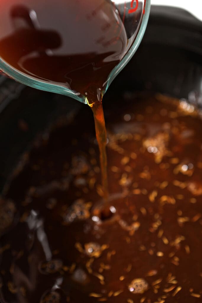 Beef stock pours into a slow cooker