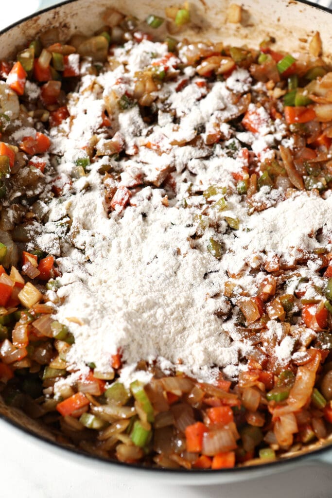 Flour sprinkled on top of cooked veggies in a skillet