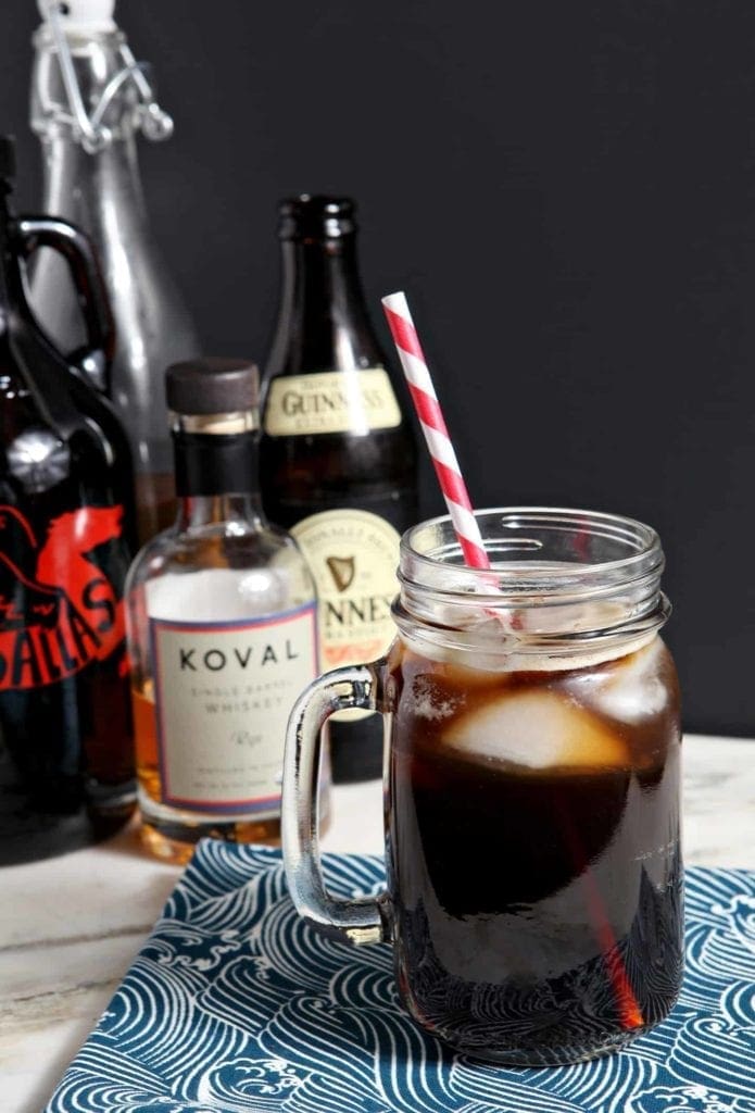 The Boyfriend Irish Coffee photographed on a light marble surface with a black background, surrounded by its ingredients