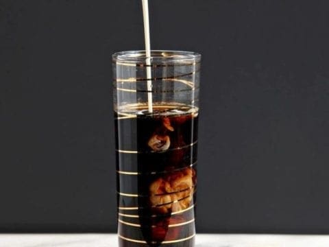 Cream pours into a coffee drink in a gold striped champagne flute