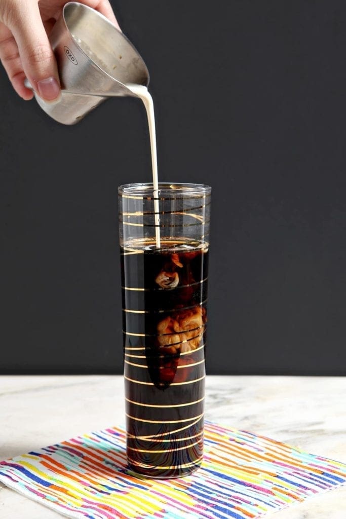 Cream pours into a coffee drink in a gold striped champagne flute