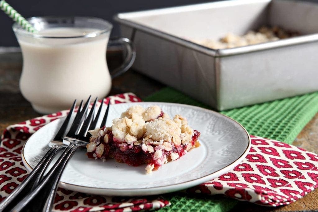 Close up of Cranberry Crumb Bar on plate with forks and glass of milk 