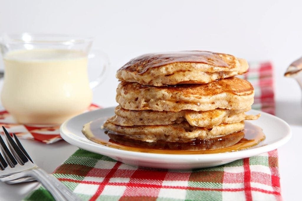 Cinnamon Syrup runs down the sides of a stack of pancakes sitting on a red and green plaid towel