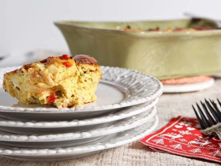A serving of Christmas Breakfast Casserole sits on a white plate with the baking dish in the background