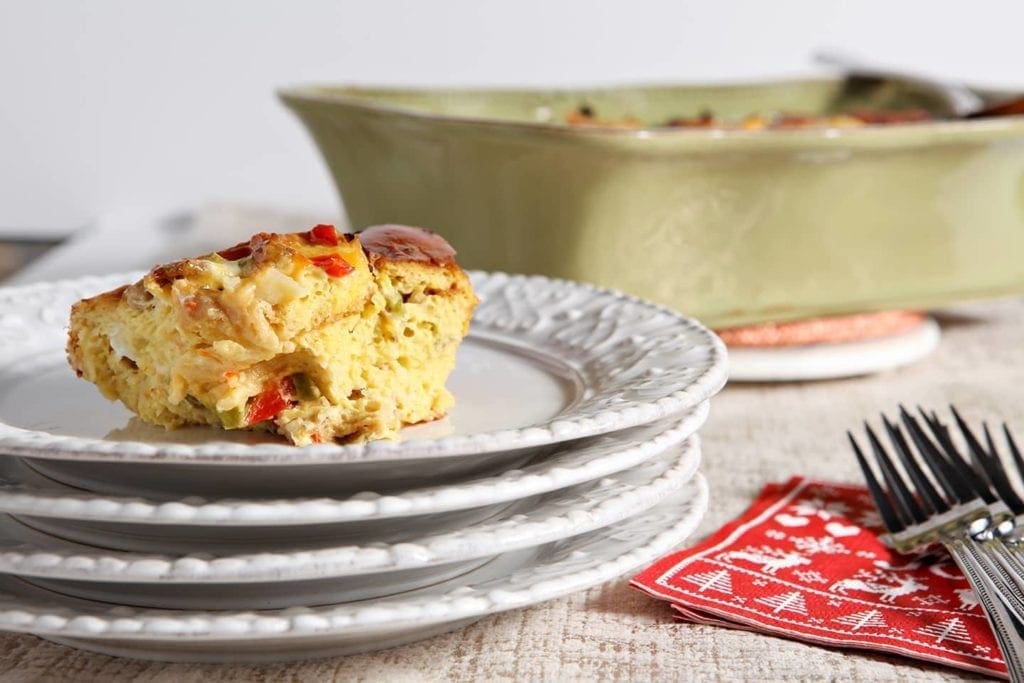 A serving of Christmas Breakfast Casserole sits on a white plate with the baking dish in the background