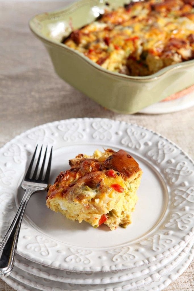 A serving of Christmas Breakfast Casserole sits on a white plate with a fork.