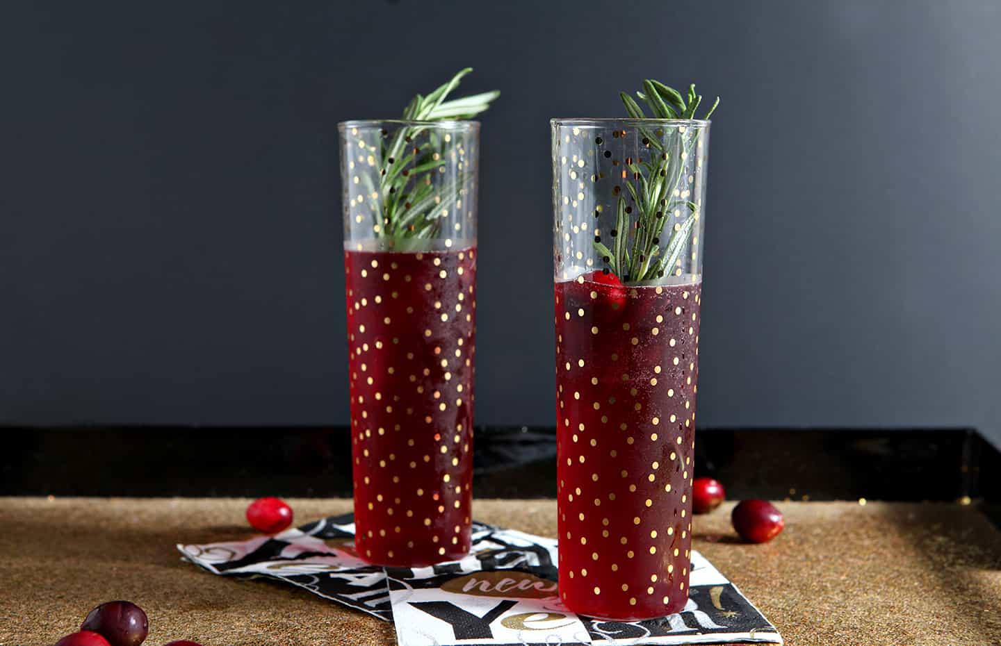 Two champagne flutes holding a cranberry bellini recipe sit on a gold glitter tray