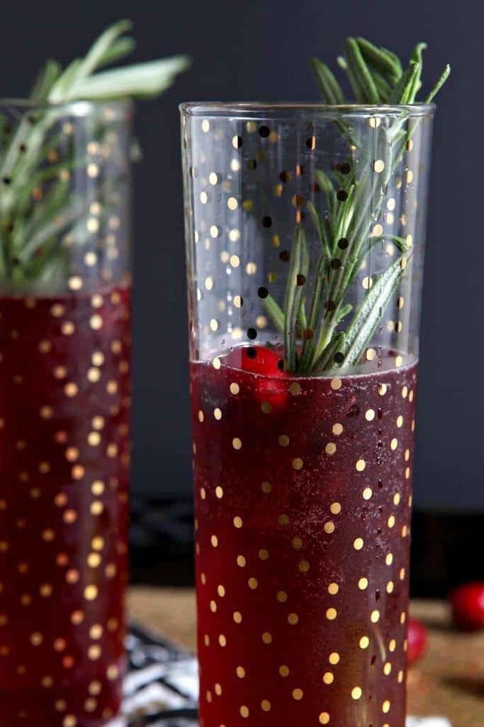 Close up of two Cranberry Bellinis, garnished with fresh cranberries and rosemary sprigs