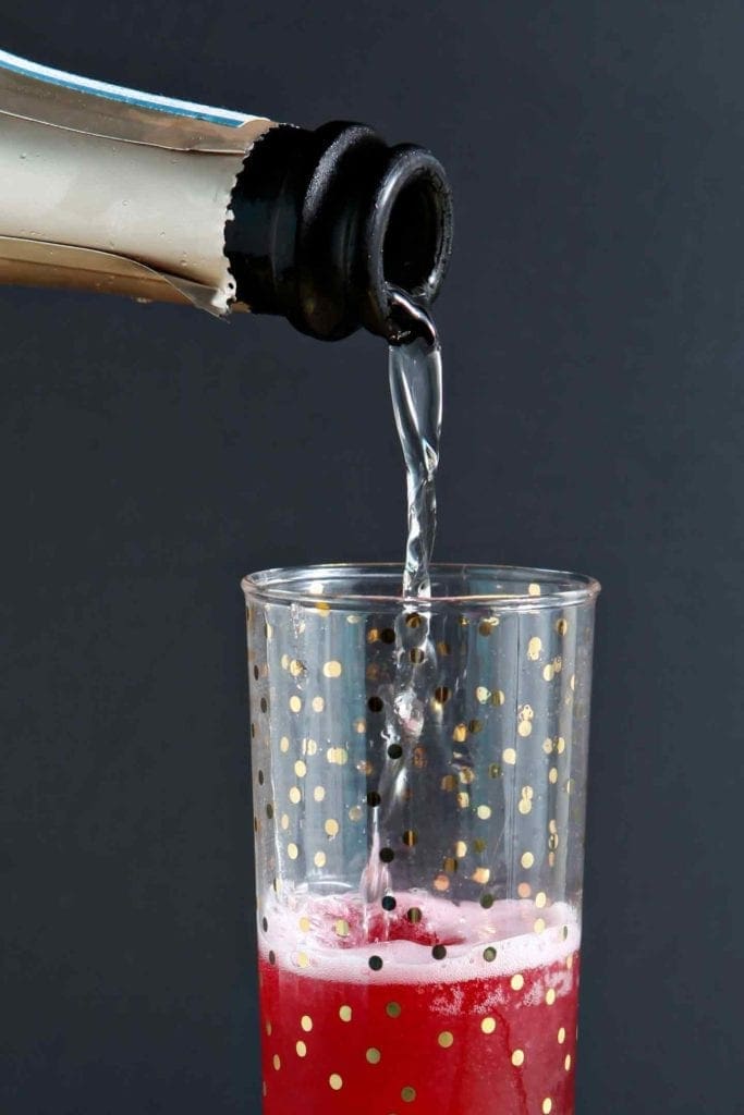 Prosecco pours into a glass holding red liquid to form a bellini recipe