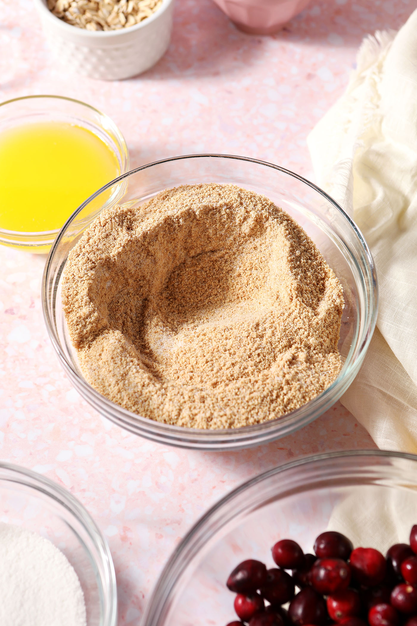 Graham cracker crumbs mixed with sugar and salt in a bowl next to bowls of other ingredients
