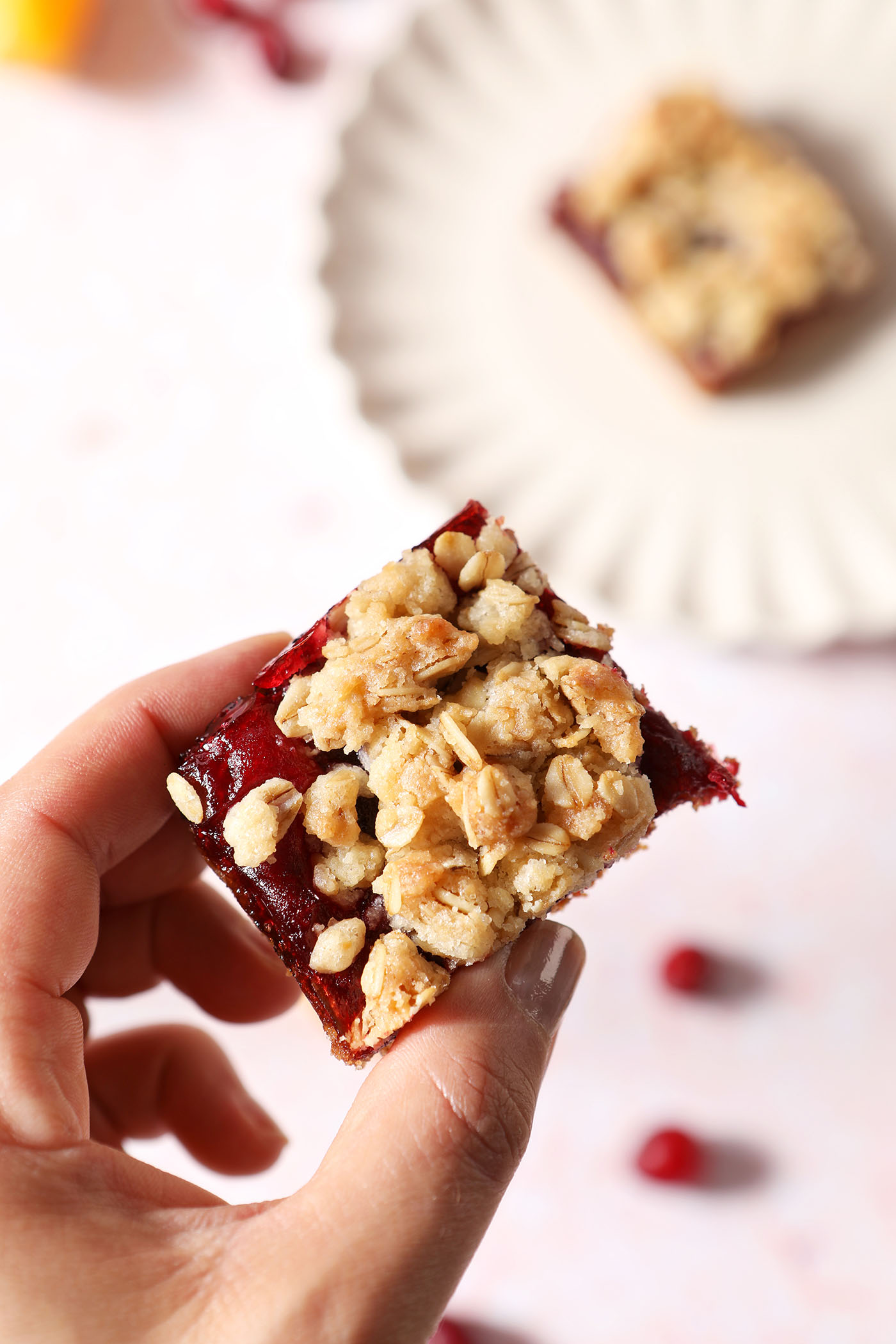 A hand holds a small cranberry crumb bar above a plate of another bar