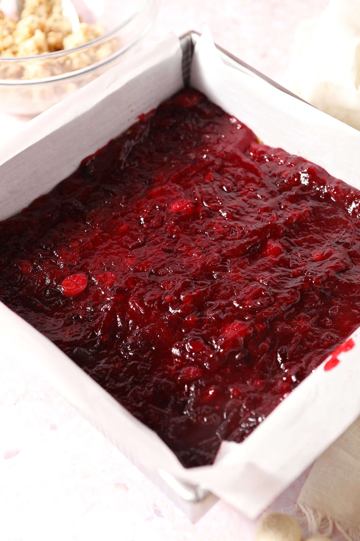 Cranberry filling on top of a crust in a square baking dish on a pink surface