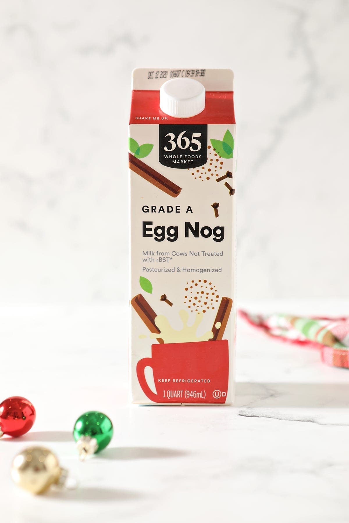 A box of 365 eggnog sits on a marble surface next to red, green and gold ornaments