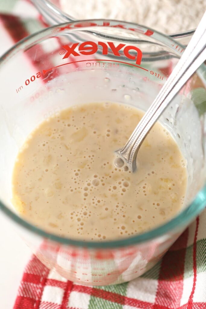 A fork mixes wet ingredients in a measuring cup on top of a green and red plaid kitchen towel