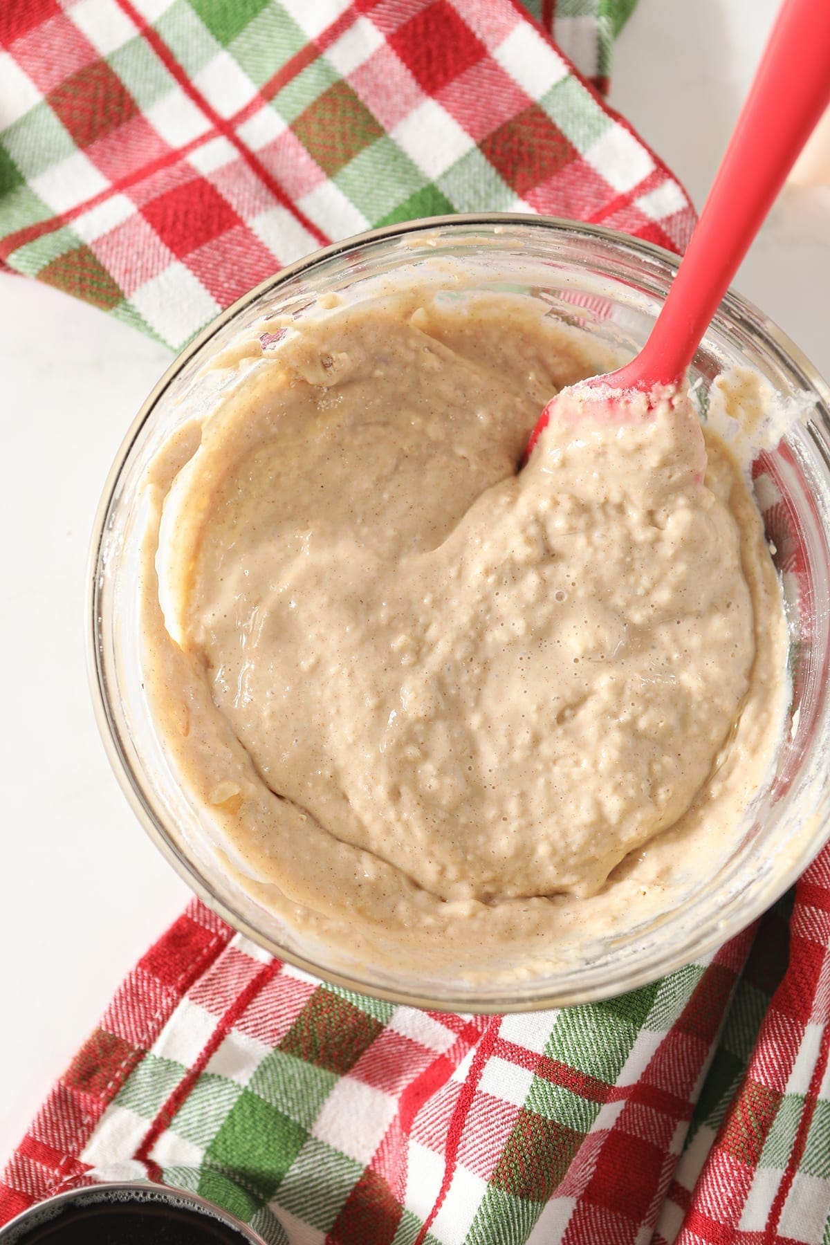 The final pancake batter in a glass bowl on top of a green and red plaid kitchen towel