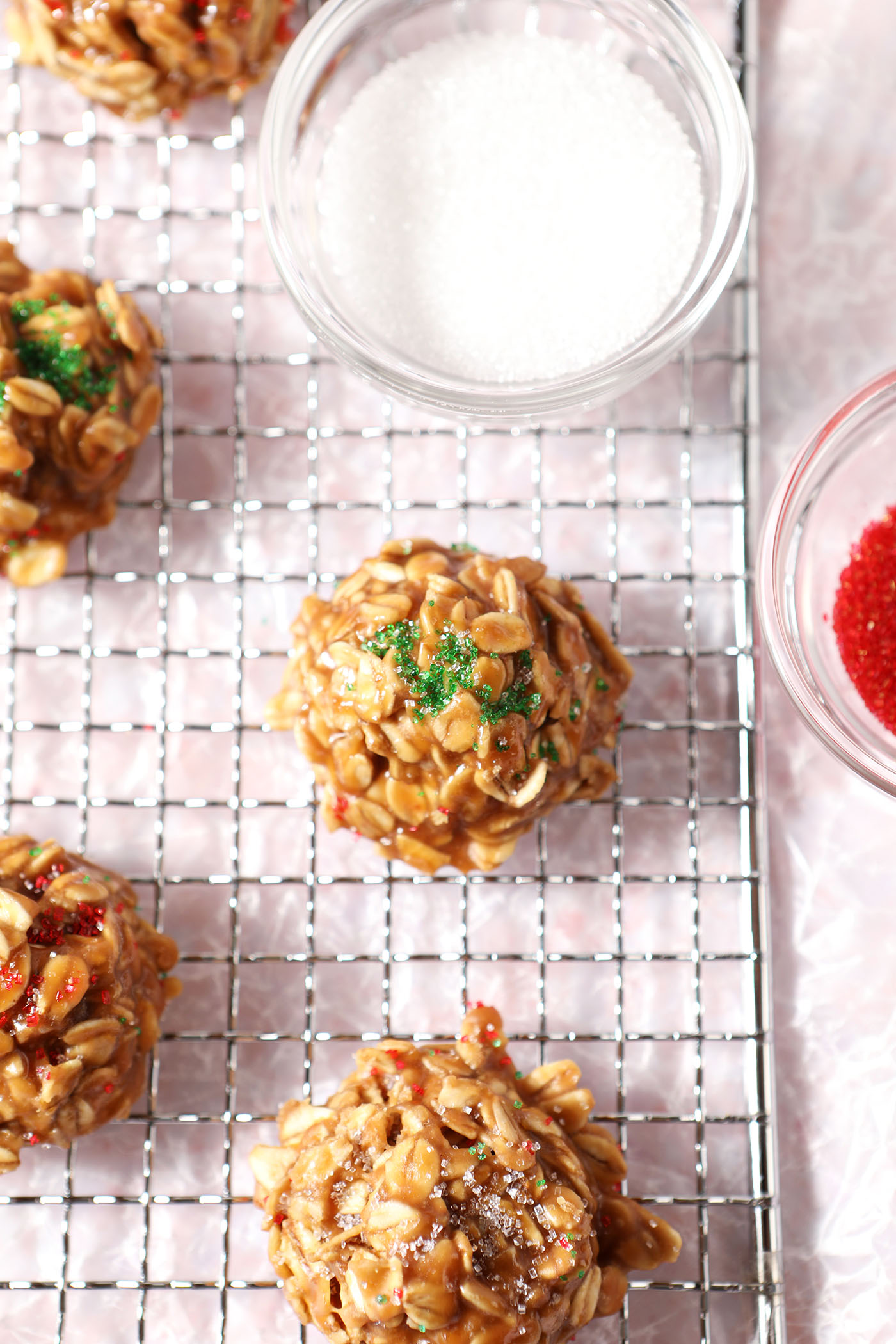 Close up of no bake cookie butter cookies on a wire rack next to colored sugars over a pink terrazzo surface